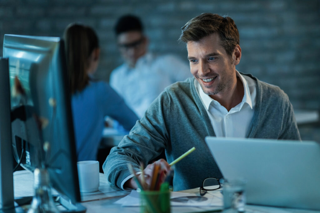 Homem sorrindo para a tela de computador em um escritório